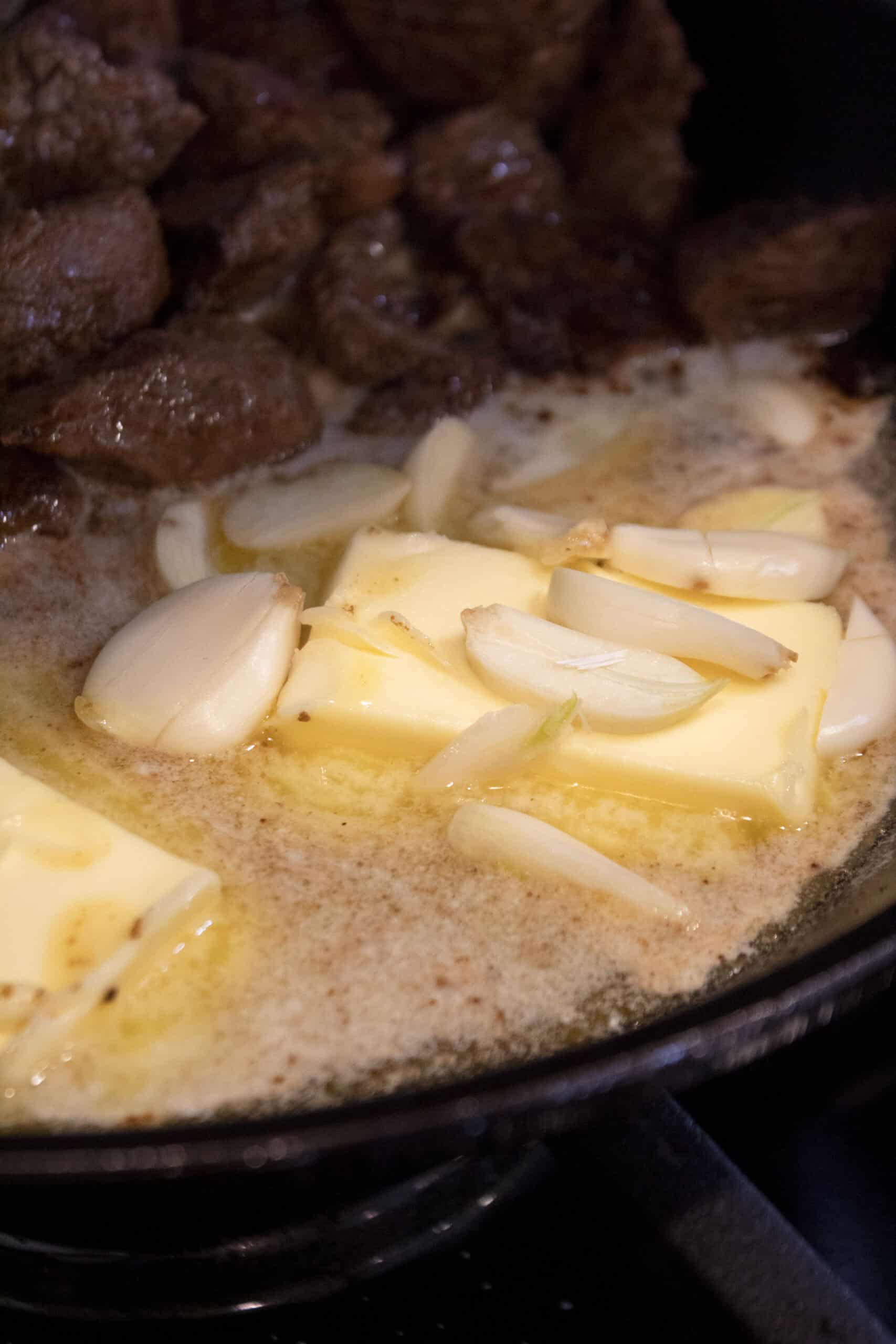 Melted butter with sliced garlic in a cast iron with seared steak tips.
